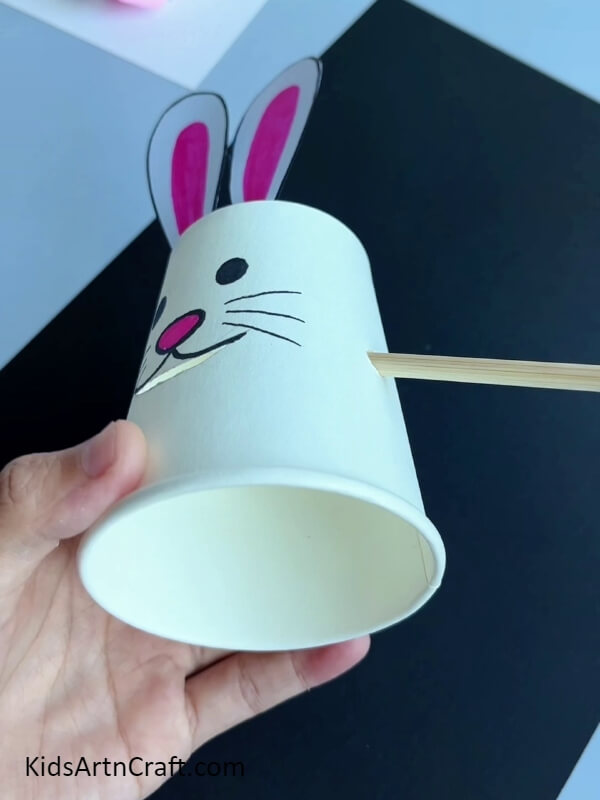 Making Holes And Inserting A Wooden Stick- The delightful craft of a paper cup bunny eating a carrot is perfect for kids.